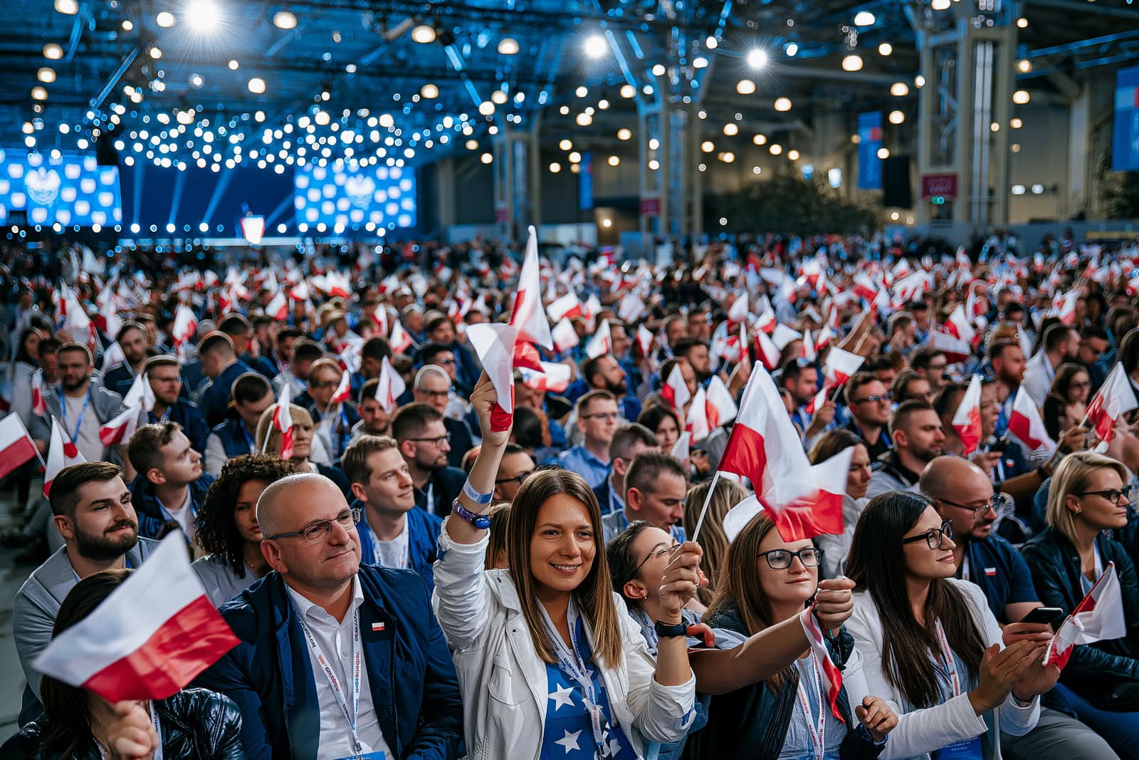 Prepuna izložbena dvorana maše malim zastavama pod jakim osvjetljenjem na početku kampanje AfD-a u Magdeburgu, s pozornicom u daljini.