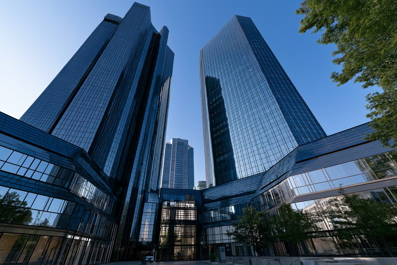 Dva staklena bankarska tornja u Frankfurtu blistaju naspram jarkoplavog neba gledana odozdo.