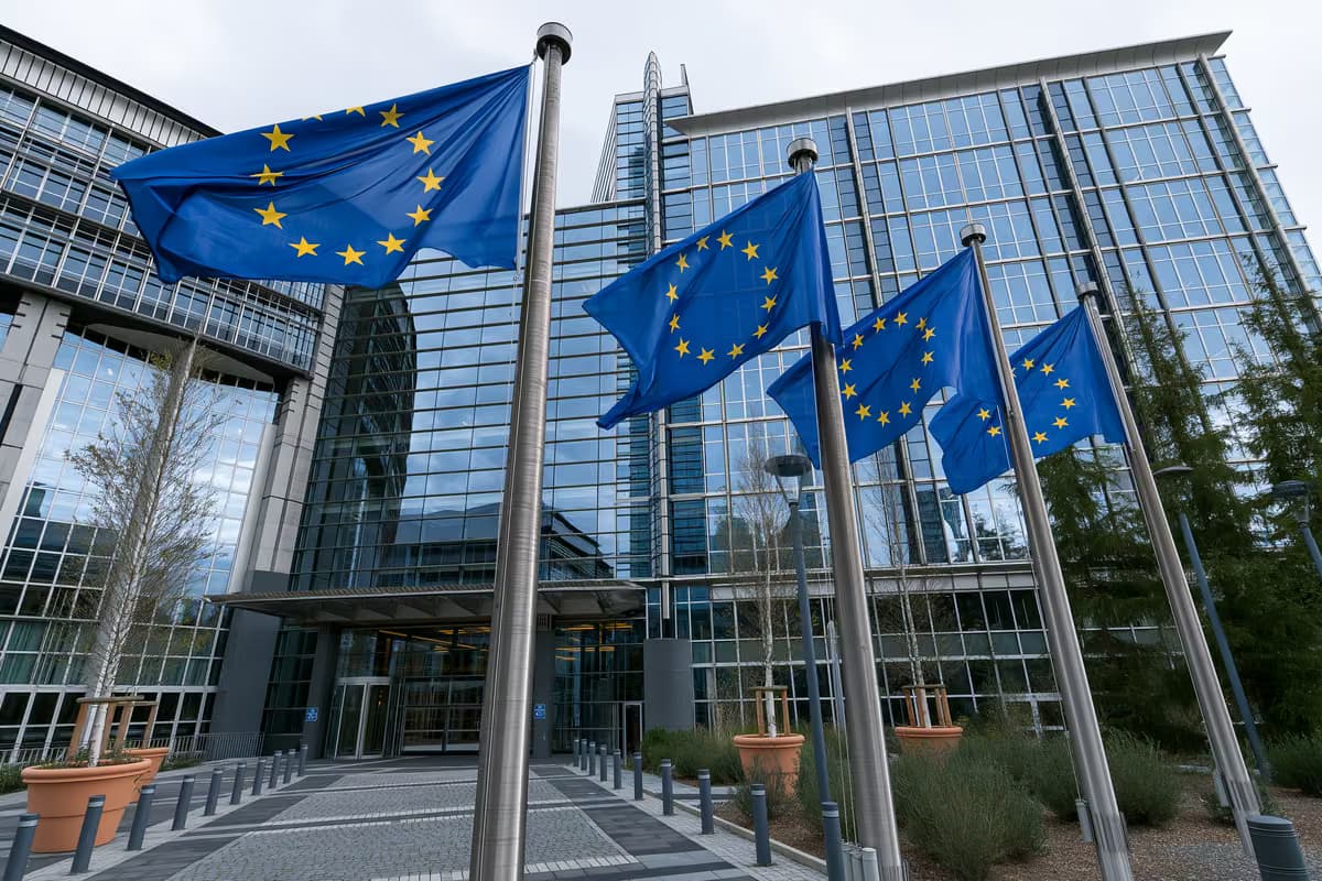 Zastave Europske unije na jarbolima ispred moderne staklene zgrade.