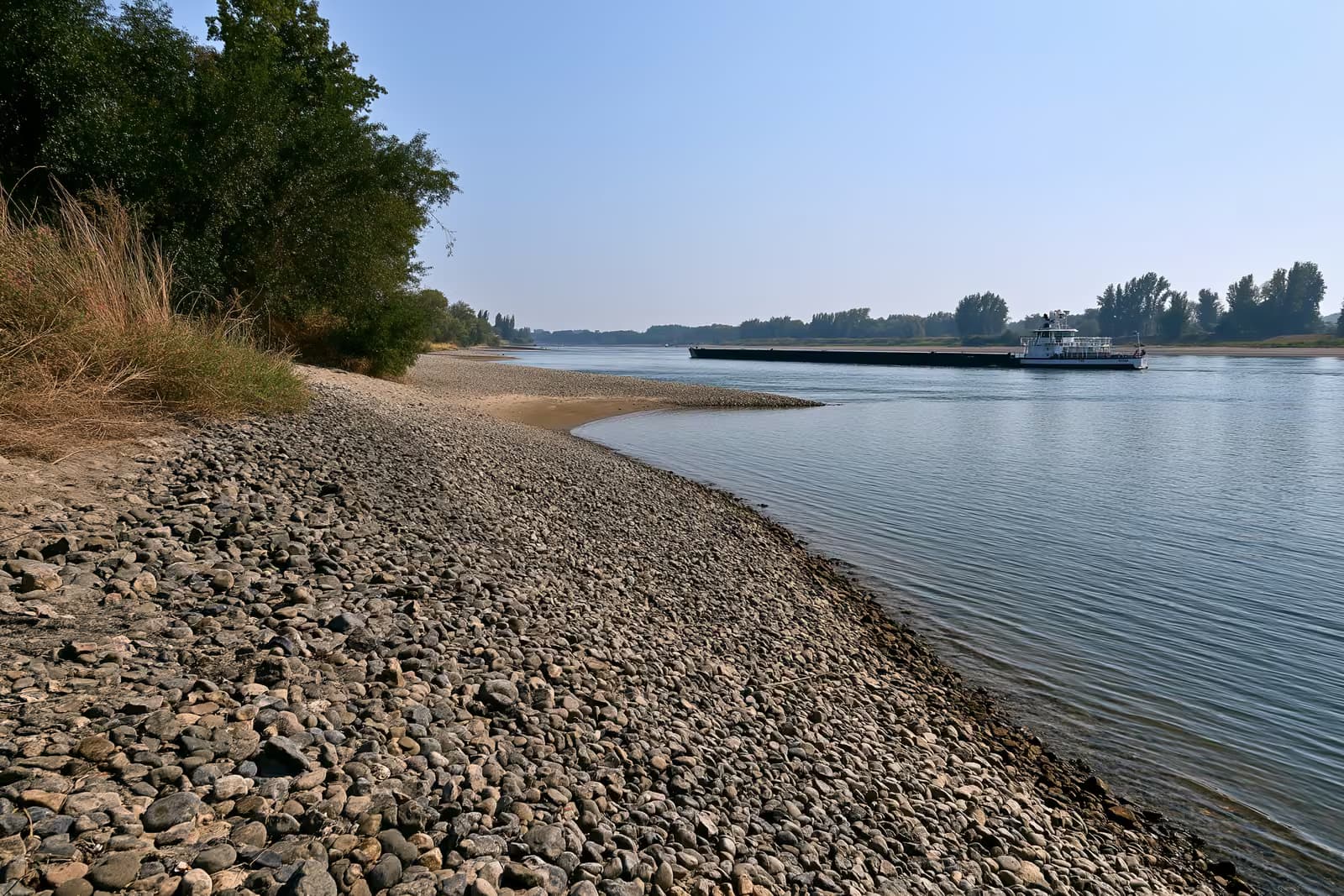 Teretna barža nisko i lagano natovarena na smanjenoj rijeci Rajni s izloženim pješčanim sprudovima.